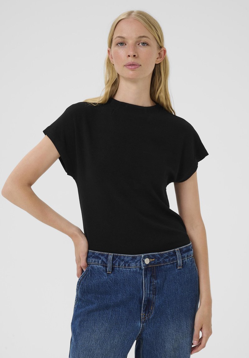 Čierny krátky rukáv top s okrúhlym výstrihom, v kombinácii s modrými džínsami. Hladká látka s voľným strihom bez viditeľných vzorov alebo ozdôb.