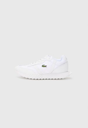 White low-top sneaker with lace-up design, textured sole, and green Lacoste crocodile logo on the side.