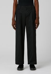 Black wide-leg trousers made from smooth fabric; features front pleats, side pockets, and a relaxed fit. No visible embellishments.