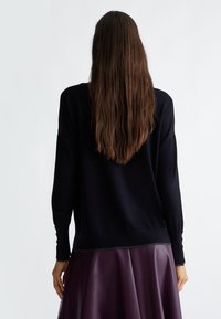 Jersey negro de punto con mangas largas, corte relajado, dobladillo redondeado y detalles de botones en los puños, combinado con una falda de cuero púrpura.