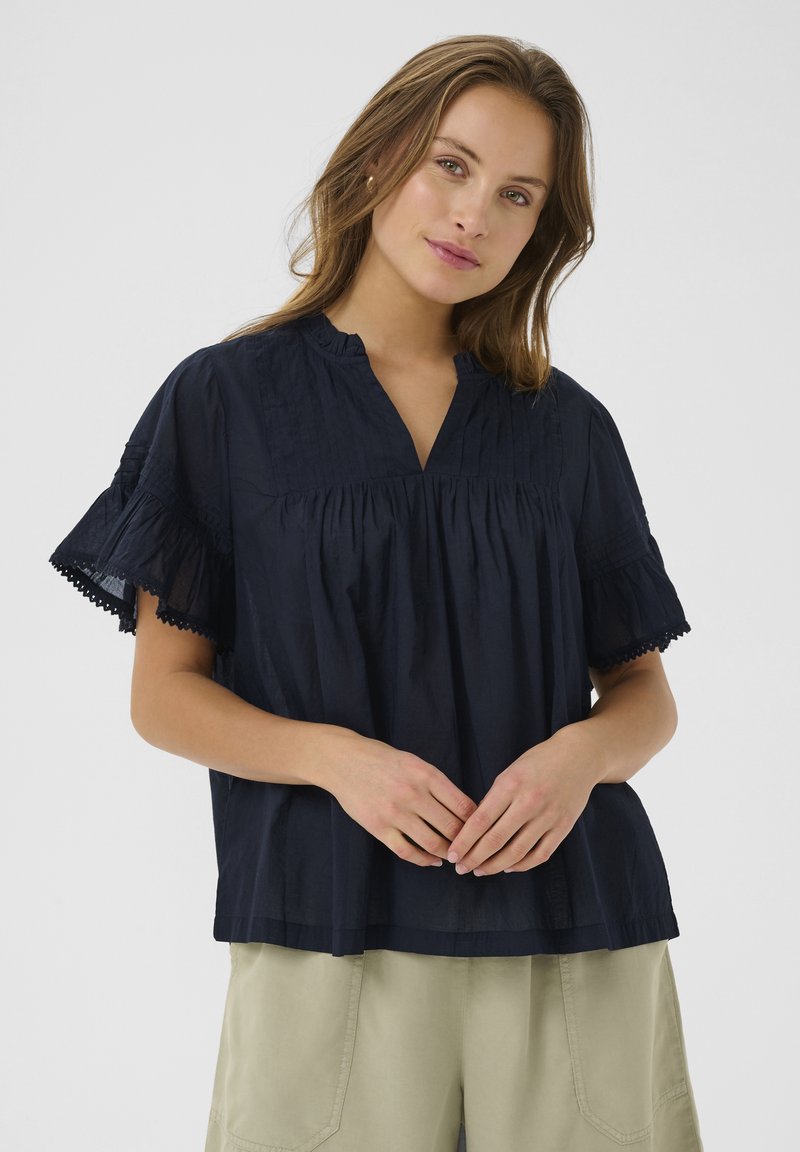 Blusa di cotone blu navy con colletto alla cinese, maniche corte a campana con dettagli in pizzo e arricciature sul busto.
