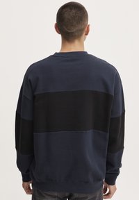 Felpa blu navy con pannelli orizzontali neri e blu. Tessuto morbido, polsini a costine e orlo a bande. Design semplice e dal fit rilassato.