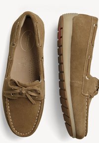 Mocassins en daim marron avec détails cousus, nœud en dentelle sur le dessus, coupe large et semelle en caoutchouc texturée, vus de dessus et de côté.