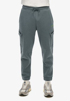 Pantalones de chándal cargo azul claro, hechos de una tela suave, con bolsillos laterales, puños elásticos y cintura ajustable con cordón. Acentuados con un logo en verde neón.