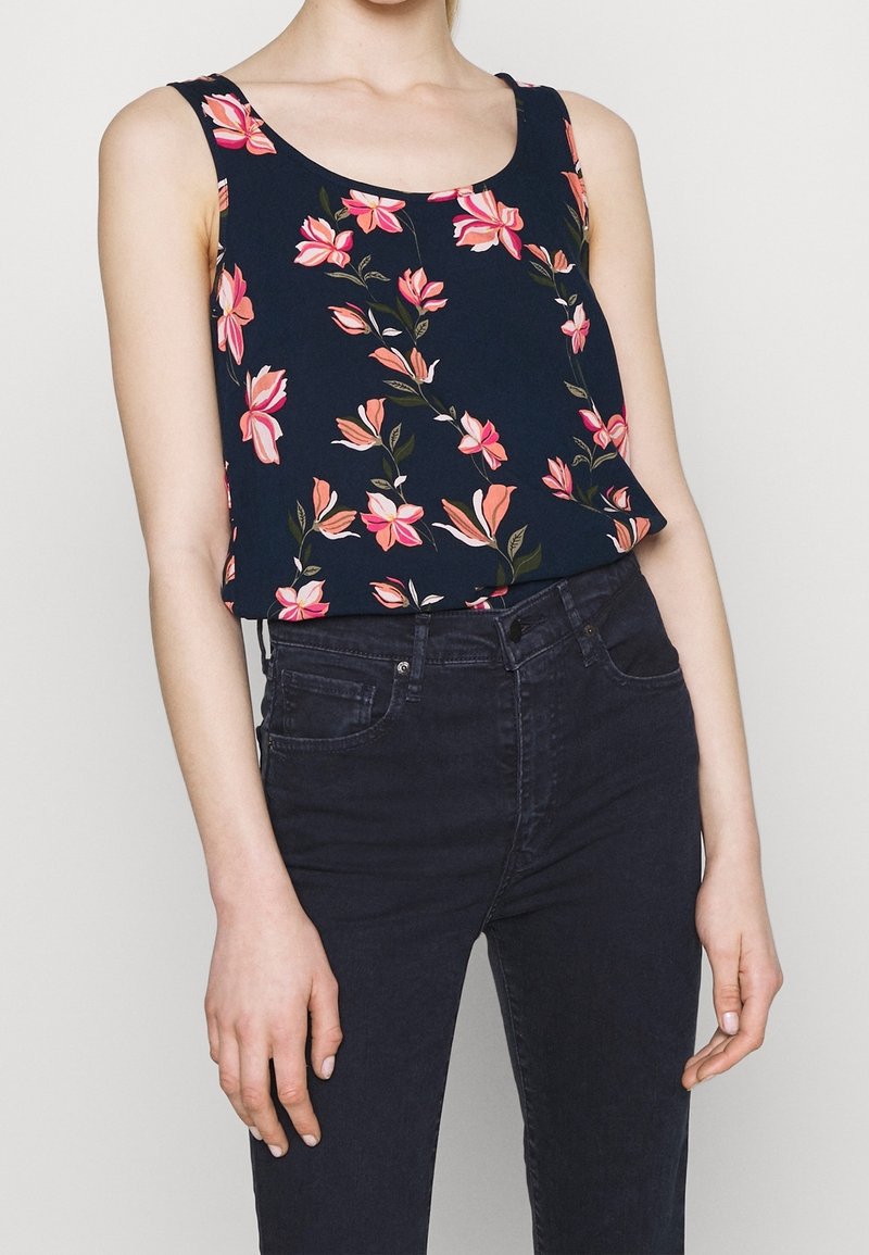 Lauluuppotoppi tummansinisellä kukkakuosilla, jossa vaaleanpunaisia ja vihreitä kukkia; pehmeä kangas, rento malli, yhdistetty tummiin farkkuihin.