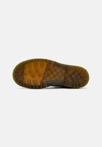 Sole of a shoe with a rugged design, featuring a textured brown rubber surface and deep grooves for traction. Semi-transparent amber accents.