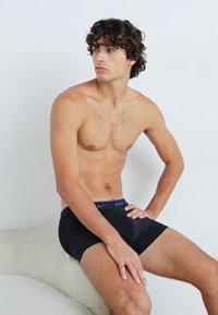 Schwarze Sportshorts aus dehnbarem Material, mit einem blauen Nike-Logo am Bund, taillierter Passform und glatter Textur.