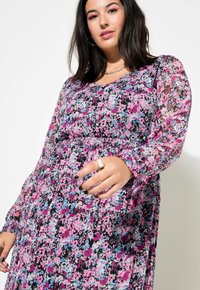 Robe fleurie avec un fond noir, ornée de fleurs roses, bleues et blanches. Manches longues et transparentes, taille cintrée et jupe fluide.