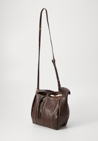 Sac à main en cuir brun avec un design décontracté, une bandoulière réglable, une fermeture supérieure à cordon et des coutures visibles sur les côtés.