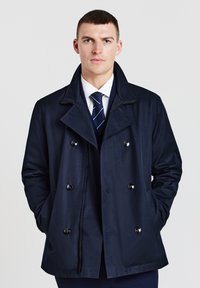 Cappotto navy a doppio petto, con bottoni grandi e tasche laterali. Tessuto liscio con colletto strutturato.