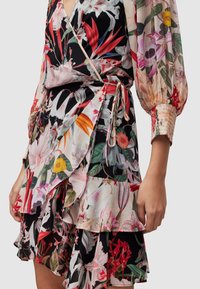 Robe portefeuille fleurie avec un ourlet court à volants ; présente une base noire, de grands motifs floraux multicolores et des manches longues smockées.