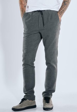 Grau, maßgeschneiderte Hose aus gewebtem Stoff mit einem Kordelzugbund, schmaler Passform und seitlichen Taschen; kombiniert mit hellgrauen, niedrigen Sneakers.
