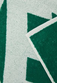 Zelené a bílé ručníky se vzorem, s texturovaným, savým povrchem. Obsahují geometrické vzory v tmavě zelené barvě na světlém pozadí.