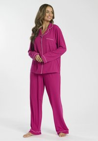 Conjunto de pijama rosa de tejido suave, que incluye una camisa con botones y un bolsillo, con detalles de ribete blanco, combinado con pantalones holgados.