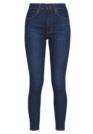 High-waisted, skinny-fit jeans in donkerblauwe denim met subtiele stikdetails en voorzakken. Zachte textuur, enkellengte ontwerp.