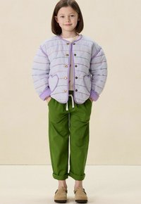 Gequilte lichtpaarse jas met meerkleurige stiksels en hartvormige zakken, gecombineerd met groene relaxte broek en beige klompen.