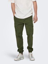 Pantalones cargo verde oliva con bolsillos laterales, puños elásticos y un corte relajado, combinados con zapatillas deportivas blancas. Se ve una camiseta blanca.