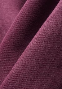 Detailný záber na textúrovanú zloženú látku v hlbokom slivkovom odtieni s viditeľným jemným pleteným vzorom a jemnými tieňmi.