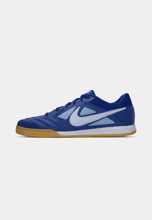 Chaussure de football en salle Nike bleu et bleu clair avec logo swoosh blanc et semelle en caoutchouc couleur gomme, vue de côté sur fond blanc.