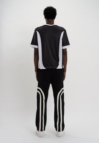 Camisola atlética preta com painéis laterais brancos e mangas curtas, combinada com calças pretas com riscas laterais brancas e cintura elástica.