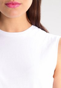 Vit bomullslös topp utan ärmar med rund halsringning, slät textur och figurnära silhuett, som visar upp en ren och enkel design.