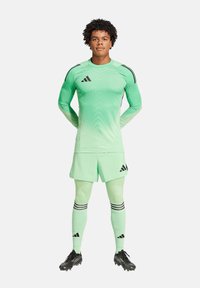 Maglia da portiere verde con design a gradiente, strisce nere, pantaloni abbinati e calze. Indossata con scarpe da calcio nere; vestibilità leggera e atletica.