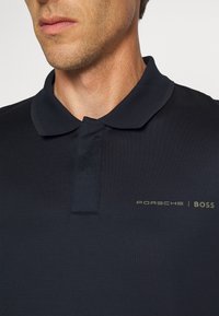 Polo-shirt marine à texture structurée, doté d'un col classique et d'un petit logo Porsche | BOSS en gris clair contrastant.