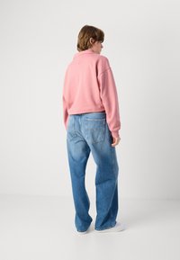 Pullover rosa corto con colletto alto, abbinato a jeans azzurri larghi. Tasche posteriori visibili e sneakers bianche semplici.