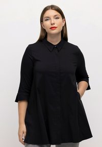 Zwarte tuniek met kraag en driekwartmouwen, zijzakken en een flared silhouet, gemaakt van een gladde stof. Knopen sluiting bij de hals.