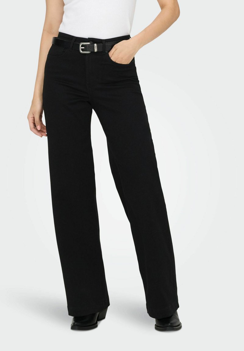 Pantalon noir à jambes larges en coton à texture lisse, doté d'une taille ceinturée et de poches avant. Porté avec un haut blanc ajusté.