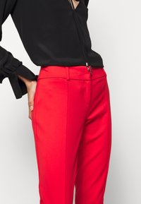 Czarna bluzka z bufiastymi rękawami i głębokim dekoltem w kształcie litery V, zestawiona z dopasowanymi, jasnoczerwonymi spodniami o gładkiej fakturze i przylegającym kroju.