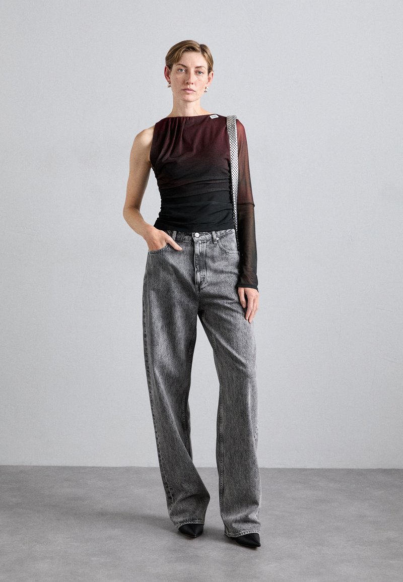 Haut asymétrique noir et bourgogne avec des manches transparentes, associé à un jean gris taille haute et des escarpins noirs à bout pointu. Détails de design simples.