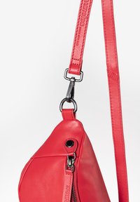 Borsa a spalla in pelle rossa con forma curva, dotata di chiusura con zip e tracolla staccabile, impreziosita da dettagli in metallo nero lucido.