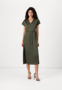Olivenfarget midikjole med V-hals, korte cap sleeves, belte i livet og en sideslitt for økt flyt og bevegelse.