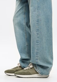Jeans azzurri chiari con vestibilità ampia, abbinati a sneakers in mesh verde e suede con suola bianca e lacci grigio chiaro.