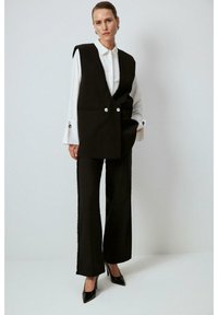 Black tailored vest with dual buttons, paired with wide-leg black trousers featuring accent stitching. The model wears a white shirt underneath.