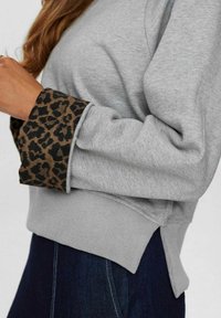 Sivá mikina s rebrovaným lemom a leopardími manžetami, so voľným strihom a bočnými rozparkami pre pohodlný pohyb.