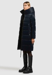 Giubbotto di piumino blu navy con colletto alto, trapuntatura orizzontale e tasche laterali con zip. Abbinato a stivali neri alti e collant neri.