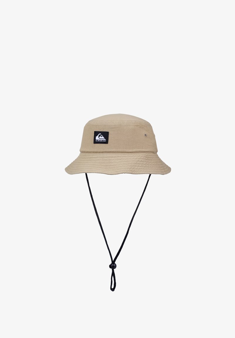 Beżowy kapelusz typu bucket wykonany z tkaniny, z czarną naszywką z logo, szerokim rondem oraz regulowanym czarnym paskiem pod brodą zapewniającym pewne dopasowanie.