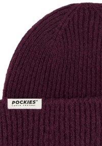 Burgunderfarget strikket lue med teksturert ribbemønster, med en hvit etikett foran med "POCKIES" og "COUCH COUTURE".