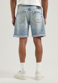 Hellblaue Jeanskurze mit umgeschlagenem Saum, zwei Gesäßtaschen und mittelhoher Passform. Dezente Ausbleichungen und Nähdetails sind sichtbar.