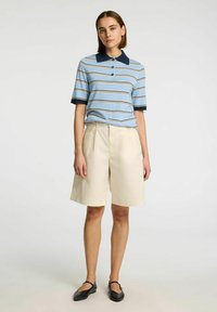 Pruhované polo triko ve světle modré barvě s námořnickými límcem a manžetami, spárované s béžovými šortkami, které mají dvě přední kapsy a volný střih.