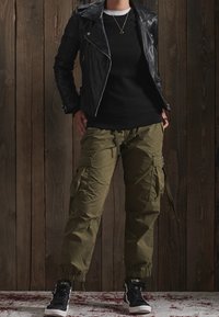 Chaqueta de motociclista de cuero negra sobre un suéter negro, combinada con pantalones cargo verde olivo y zapatillas negras con acentos blancos.