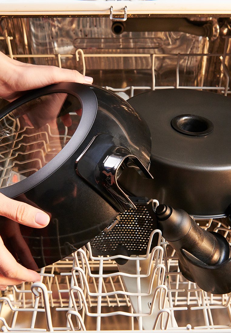 Schwarze Teile von Küchengeräten, einschließlich eines runden Sockels und eines Griffs mit einem klaren Deckel, die im Geschirrspüler-Rack positioniert sind.