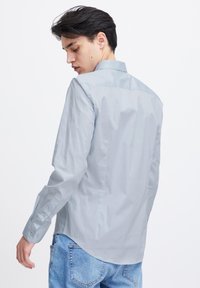 Lichtblauw overhemd met lange mouwen en een button-down kraag, zachte textuur, en een iets gebogen zoom, gedragen met denim jeans.