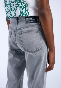 Jeans de mezclilla gris con cintura alta, corte recto y dos bolsillos traseros. La etiqueta en la cinturilla muestra el logotipo de la marca y la información.