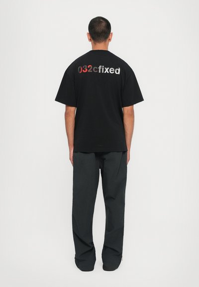 Black t-shirt with short sleeves featuring "032cfixed" printed in red and silver on the back; worn with dark gray pants.