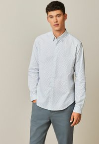 Lyseblå skjorte med knapper, præget af et geometrisk mønster, lange ærmer og spidse kraver. Sammen med grå bukser.