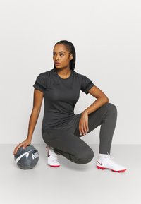 Grijze sporttop en -broek, witte en rode voetbalschoenen, houdt een grijze voetbal vast met witte en zwarte accenten. Slank ontwerp met minimale branding.