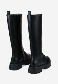 Botas negras de cuero hasta la rodilla. Cuentan con una suela gruesa, cremallera lateral y detalles de cordones en la parte frontal. Textura suave con acabado mate.